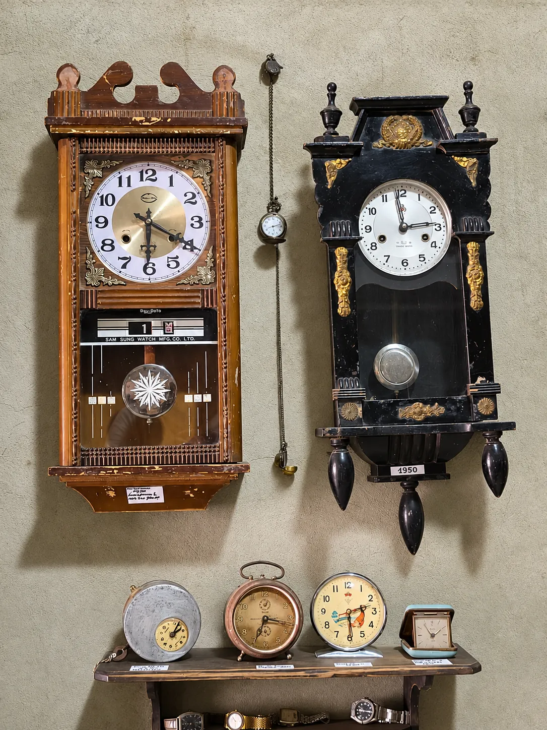 Dos relojes de pared con péndulo y cuatro despertadores antiguos sobre una repisa