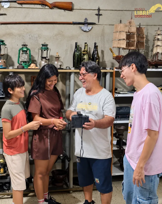 Fredy José Pinillos muestra una cámara antigua a tres visitantes jóvenes dentro del museo