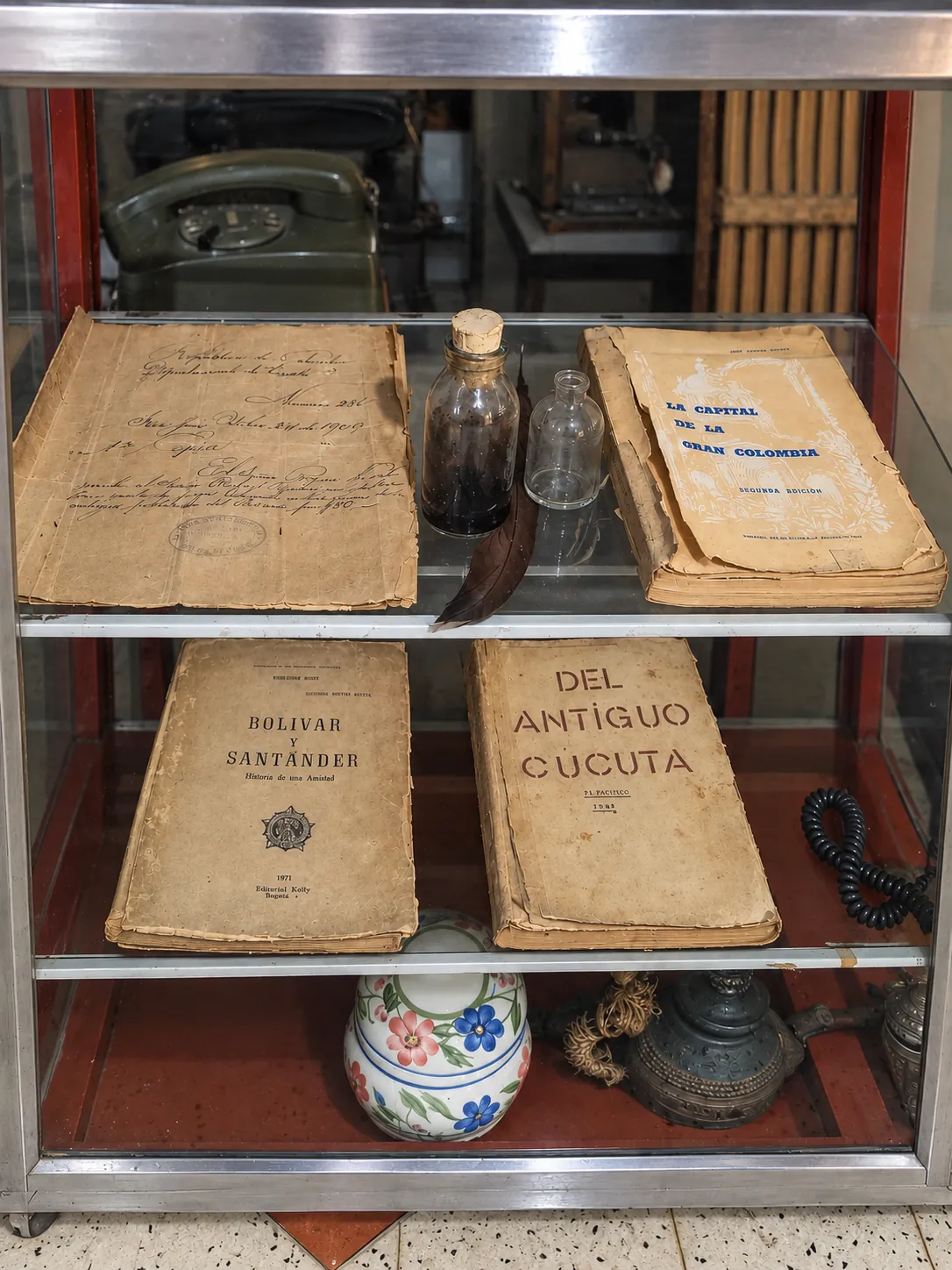 Vitrina con libros antiguos: La capital de la Gran Colombia, Bolívar y Santander y Del antiguo Cúcuta, junto a un documento manuscrito y un tintero con pluma